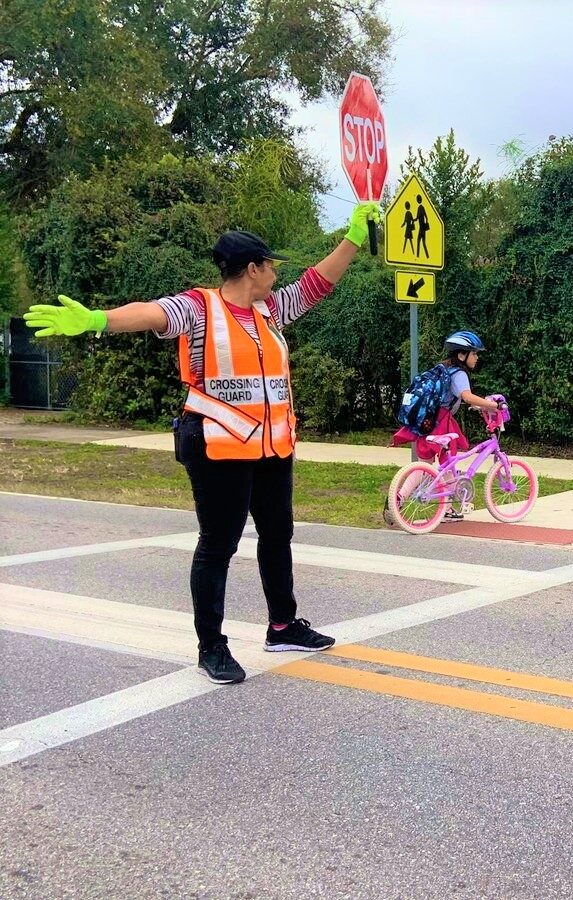 female crossing guard helping a girl with a bike cross the street